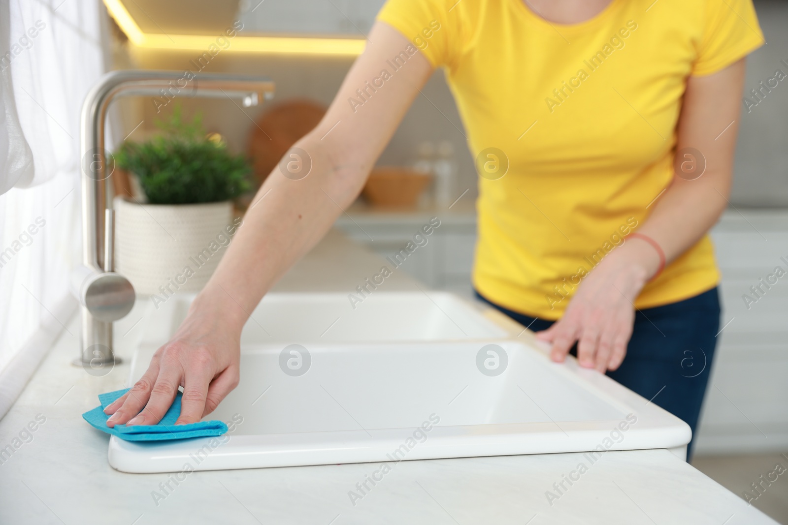 Photo of Woman wiping kitchen sink with rag indoors, closeup