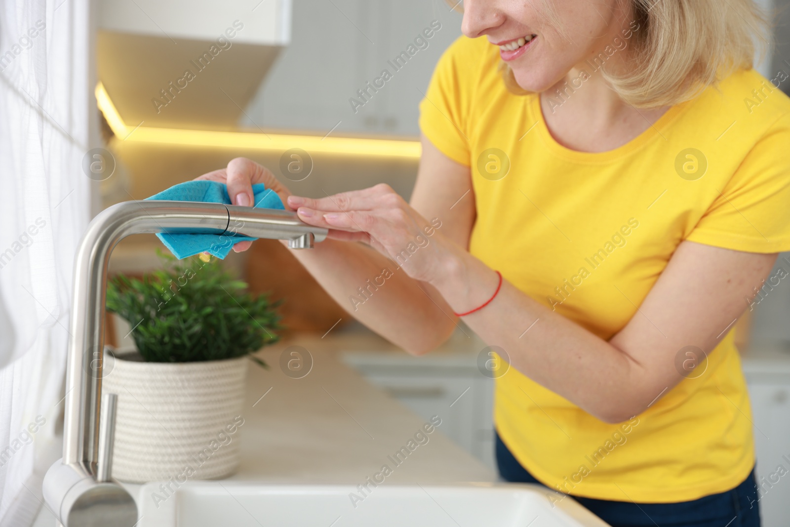 Photo of Woman wiping faucet of kitchen sink with rag indoors, closeup