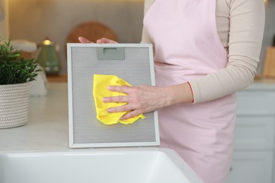 Photo of Woman cleaning filter of kitchen hood with rag indoors, closeup