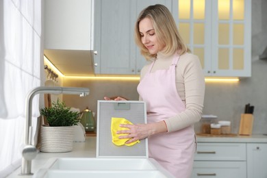 Photo of Woman cleaning filter of kitchen hood with rag indoors