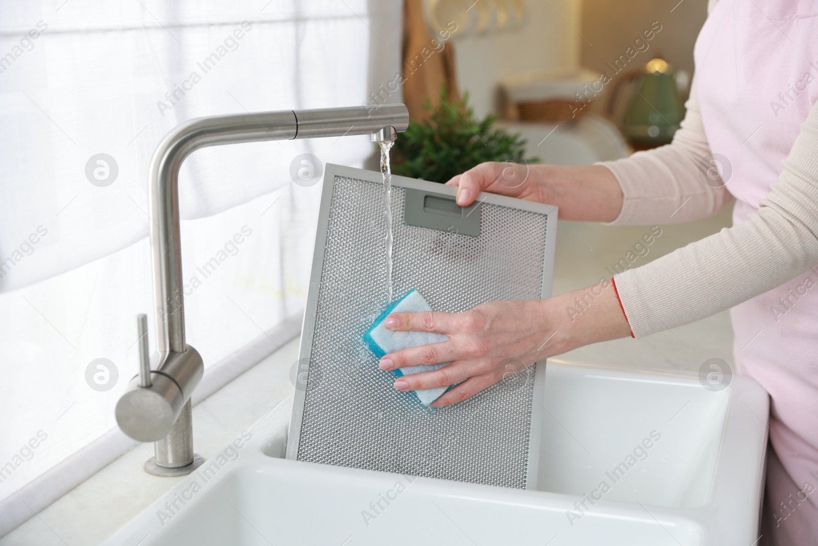 Photo of Woman washing filter of kitchen hood in sink indoors, closeup