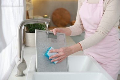 Photo of Woman washing filter of kitchen hood in sink indoors, closeup