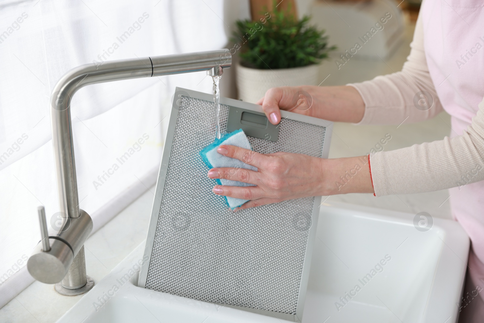 Photo of Woman washing filter of kitchen hood in sink indoors, closeup