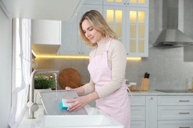 Photo of Woman washing filter of kitchen hood in sink indoors