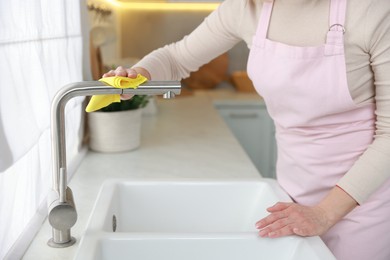 Photo of Woman wiping faucet of kitchen sink with rag indoors, closeup