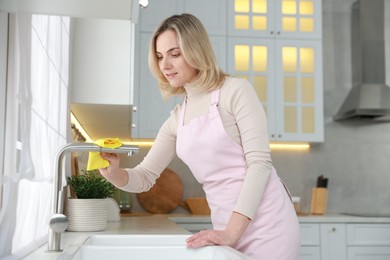 Photo of Woman wiping faucet of kitchen sink with rag indoors