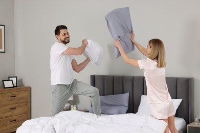 Photo of Couple having pillow fight while changing bed linens at home