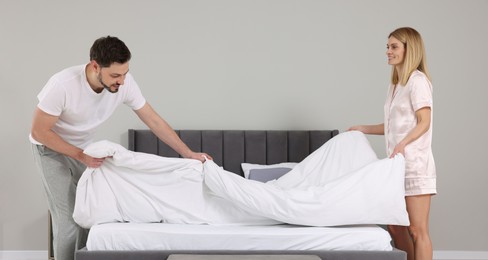 Photo of Couple changing bed linens in room. Domestic chores