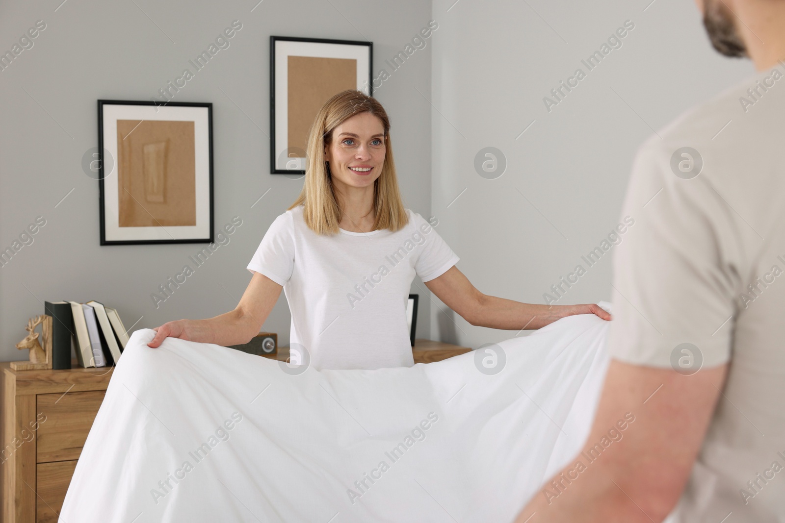 Photo of Couple changing bed linens in room. Domestic chores