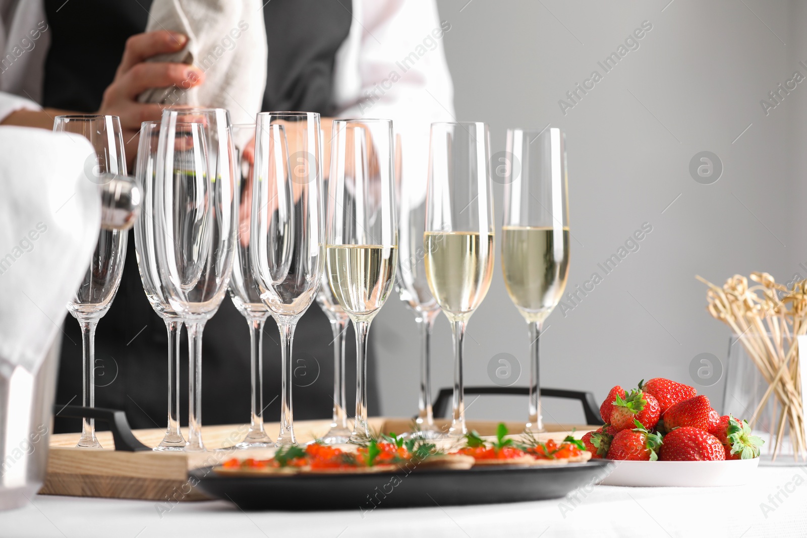 Photo of Waiter with bottle of drink, closeup. Champagne in glasses, strawberries and canapes on table