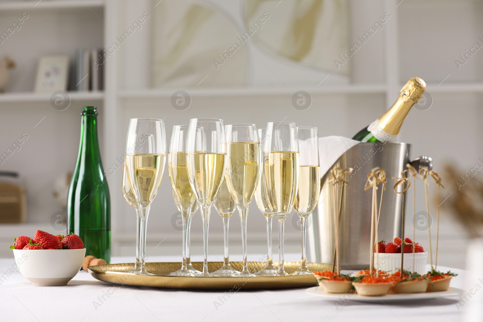 Photo of Champagne, strawberries and canapes with red caviar on white table indoors