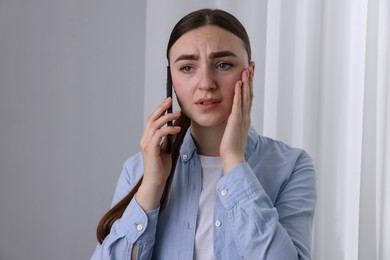 Photo of Stressed woman calling hotline for mental health help near window at home