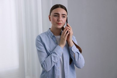 Stressed woman calling hotline for mental health help near window at home