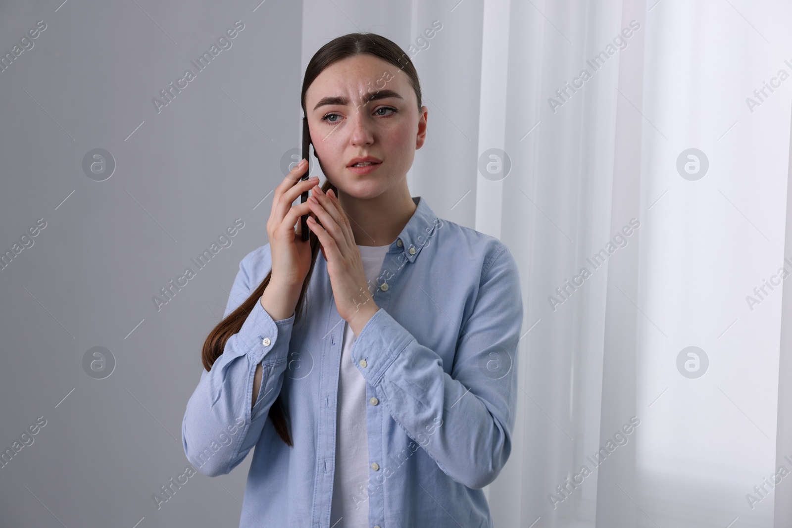 Photo of Stressed woman calling hotline for mental health help near window at home