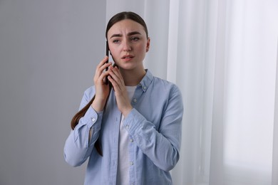 Photo of Stressed woman calling hotline for mental health help near window at home