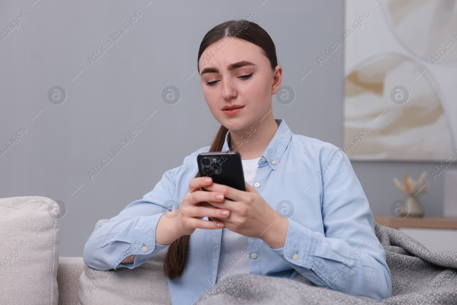 Photo of Depressed woman calling hotline for mental health help on sofa at home