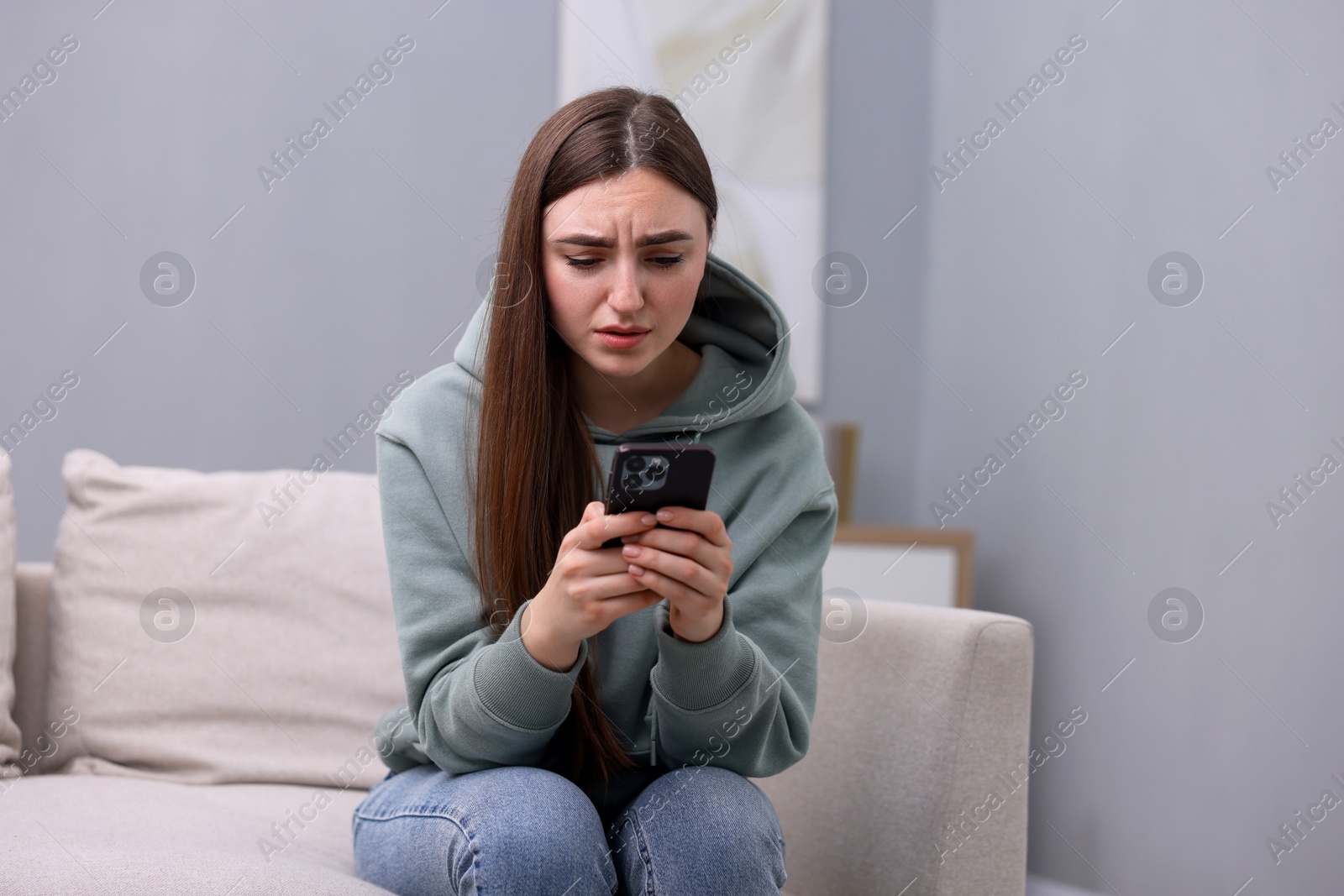 Photo of Depressed woman calling hotline for mental health help on sofa at home