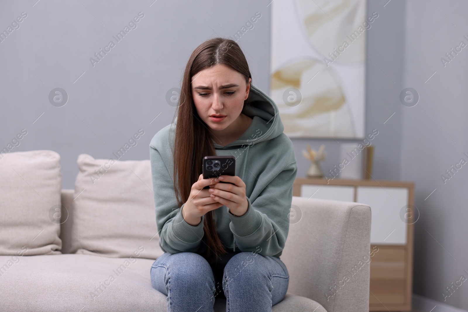 Photo of Depressed woman calling hotline for mental health help on sofa at home