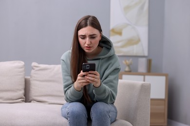 Photo of Depressed woman calling hotline for mental health help on sofa at home