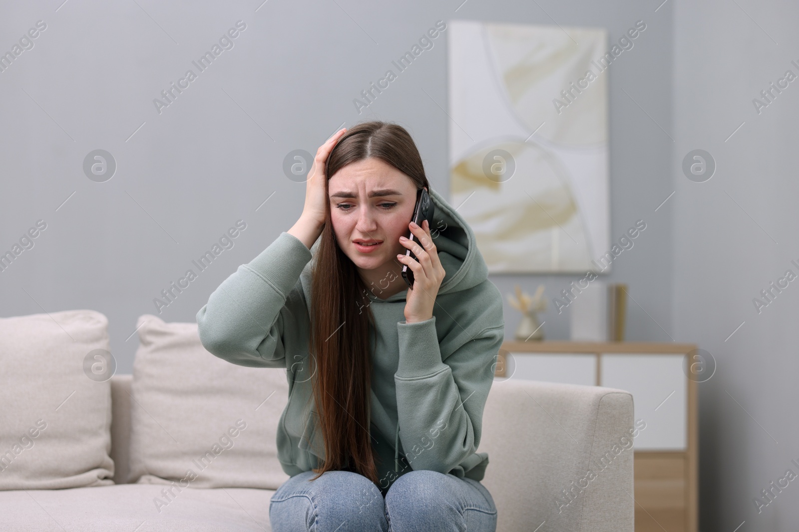 Photo of Depressed woman calling hotline for mental health help on sofa at home