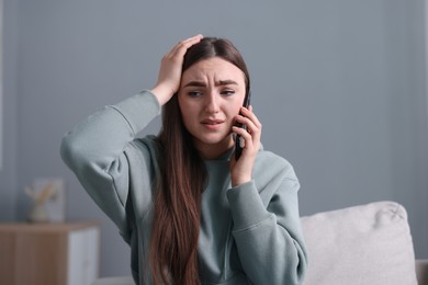 Photo of Depressed woman calling hotline for mental health help on sofa at home