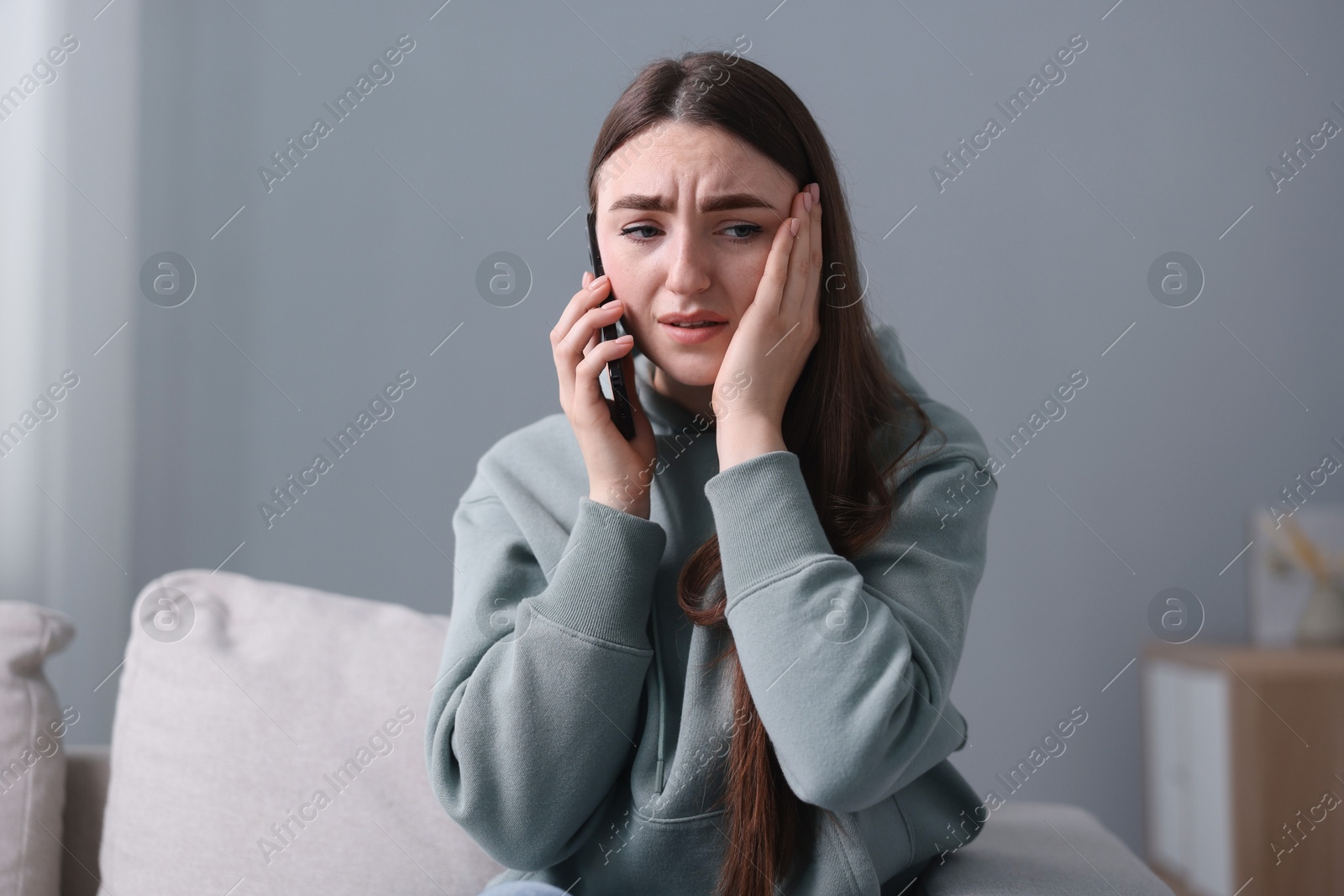 Photo of Depressed woman calling hotline for mental health help on sofa at home