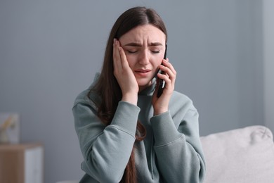 Photo of Depressed woman calling hotline for mental health help on sofa at home