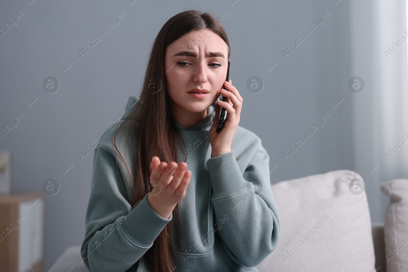 Photo of Depressed woman calling hotline for mental health help on sofa at home