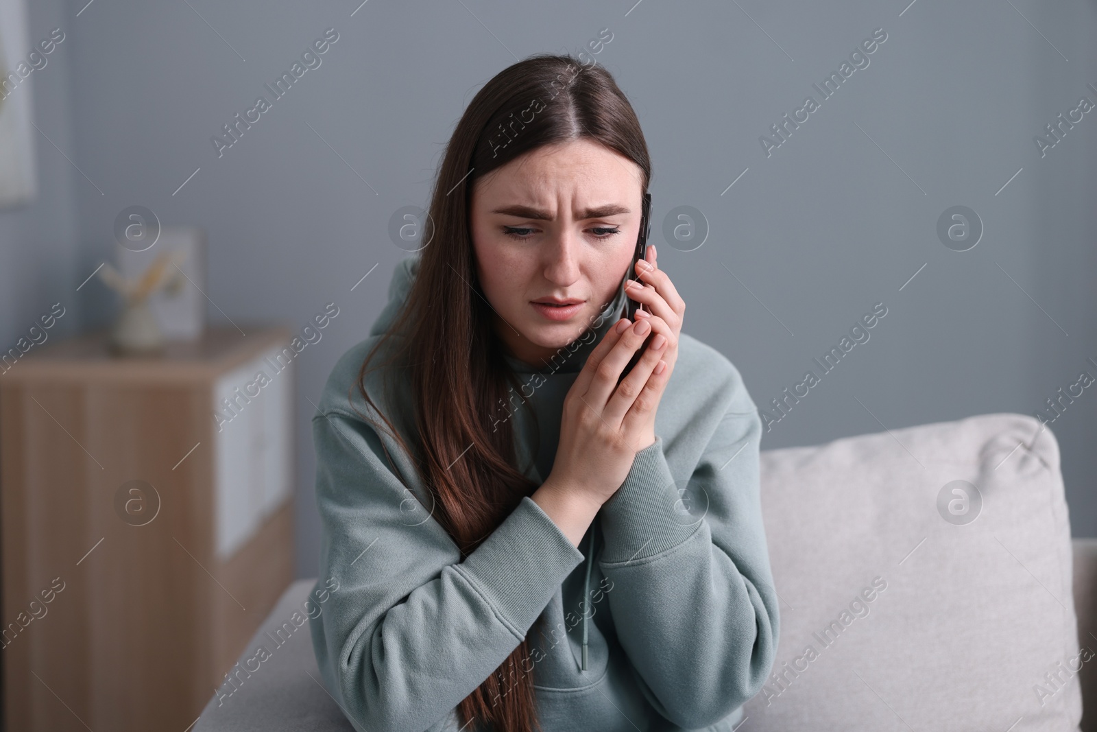 Photo of Depressed woman calling hotline for mental health help on sofa at home