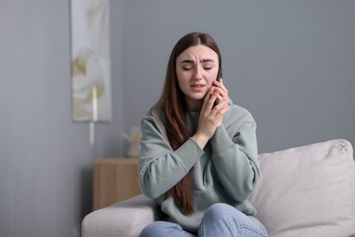 Photo of Depressed woman calling hotline for mental health help on sofa at home