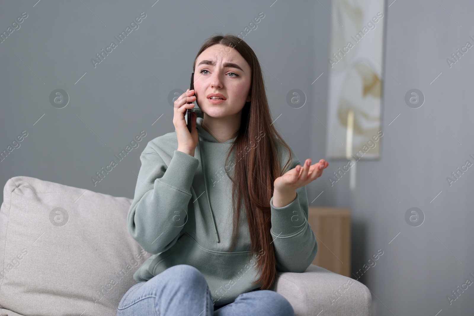 Photo of Depressed woman calling hotline for mental health help on sofa at home