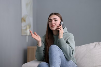 Photo of Depressed woman calling hotline for mental health help on sofa at home