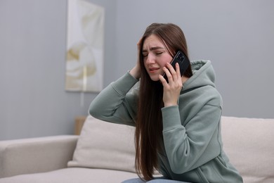 Photo of Depressed woman calling hotline for mental health help on sofa at home