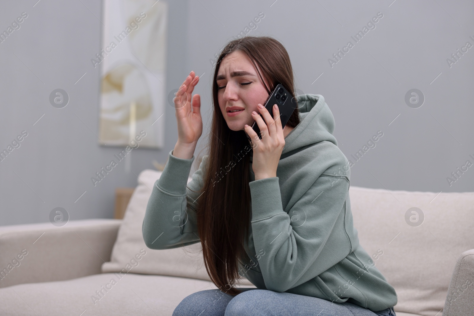 Photo of Depressed woman calling hotline for mental health help on sofa at home