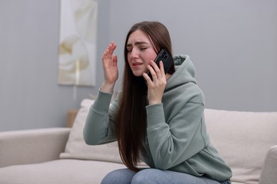 Photo of Depressed woman calling hotline for mental health help on sofa at home