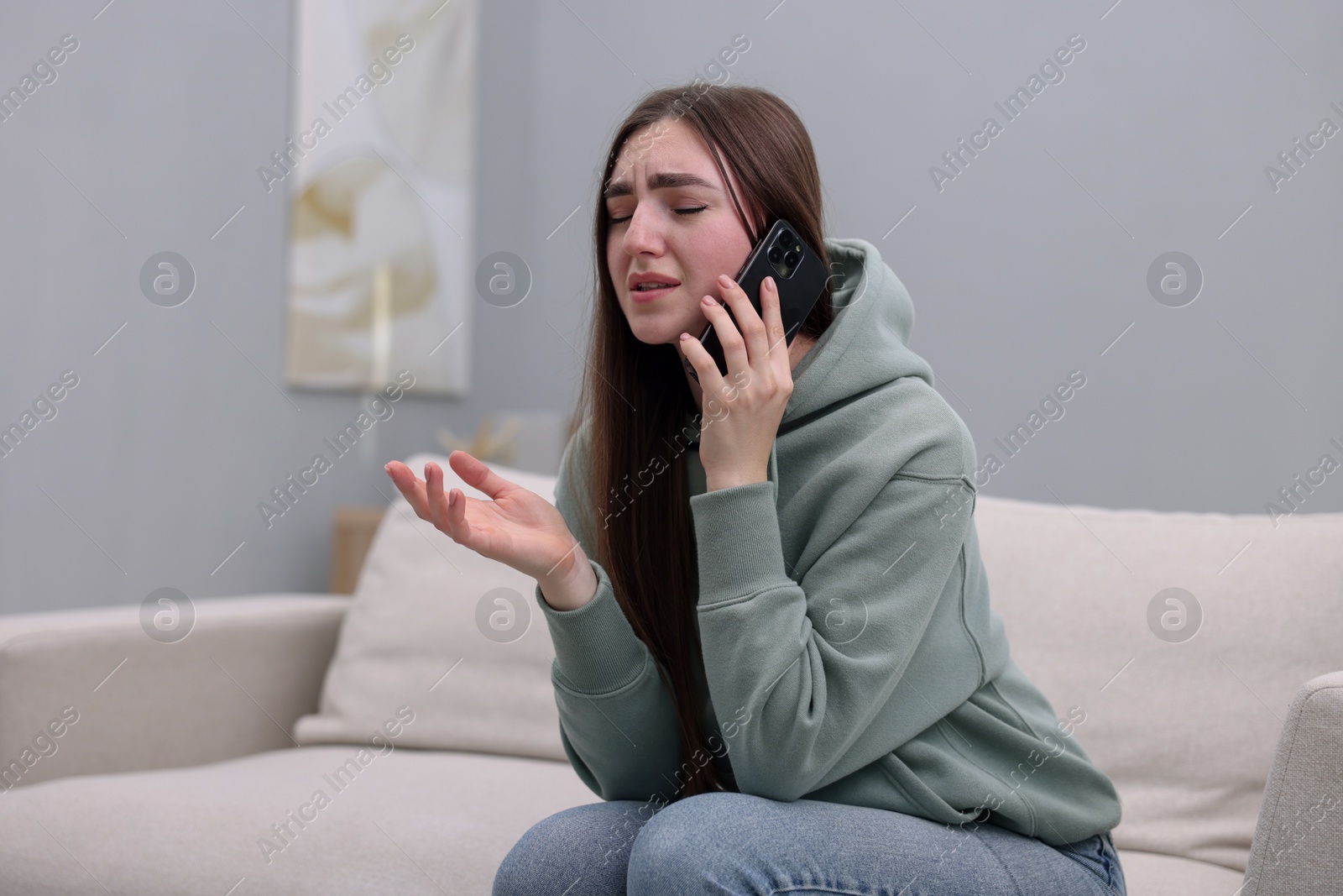 Photo of Depressed woman calling hotline for mental health help on sofa at home