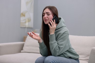 Photo of Depressed woman calling hotline for mental health help on sofa at home