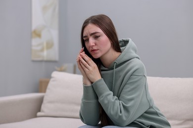 Photo of Depressed woman calling hotline for mental health help on sofa at home