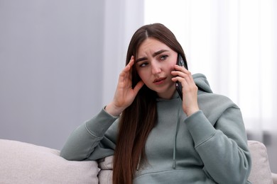 Photo of Depressed woman calling hotline for mental health help on sofa at home