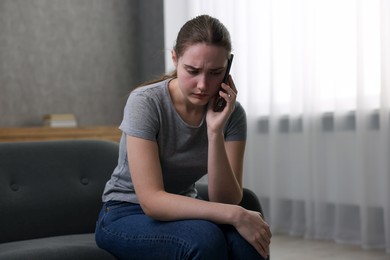 Photo of Depressed woman calling hotline for mental health help on sofa at home