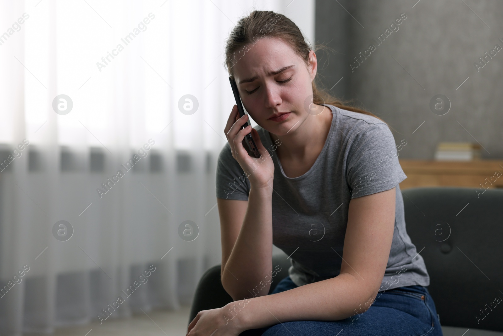 Photo of Depressed woman calling hotline for mental health help on sofa at home