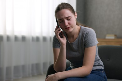 Photo of Depressed woman calling hotline for mental health help on sofa at home