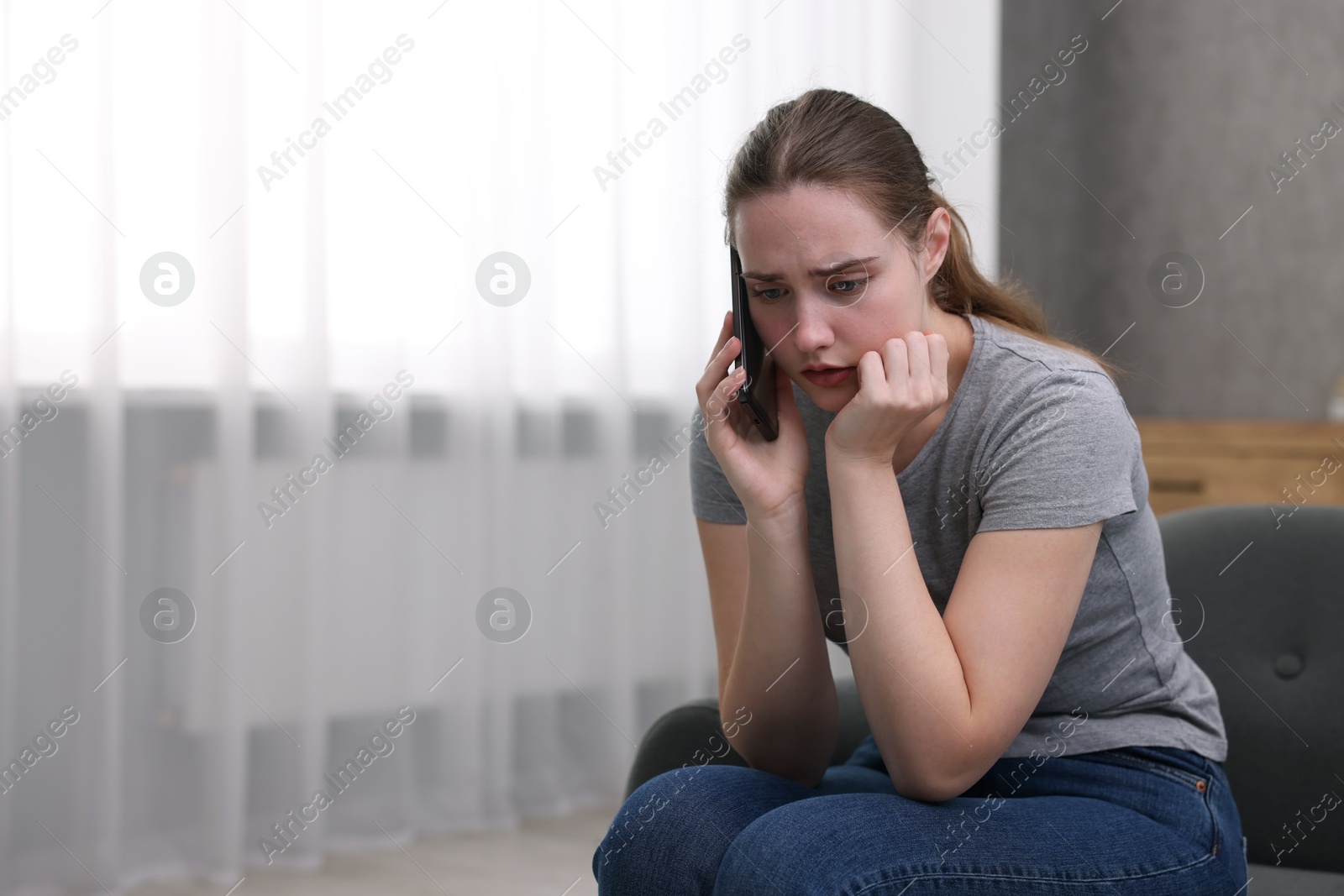 Photo of Depressed woman calling hotline for mental health help on sofa at home. Space for text