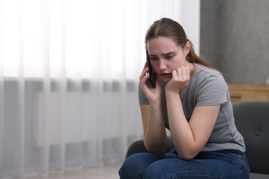 Photo of Depressed woman calling hotline for mental health help on sofa at home. Space for text