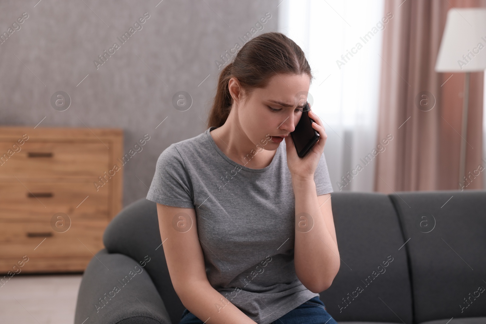 Photo of Depressed woman calling hotline for mental health help on sofa at home