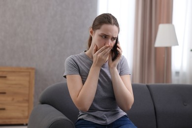 Photo of Depressed woman calling hotline for mental health help on sofa at home