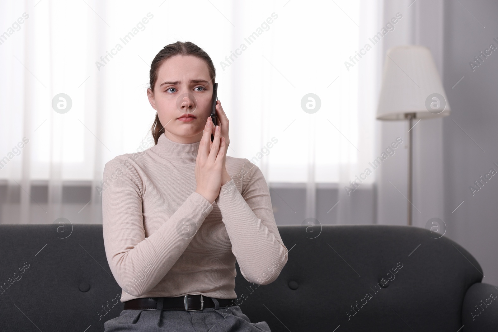 Photo of Depressed woman calling hotline for mental health help on sofa at home. Space for text