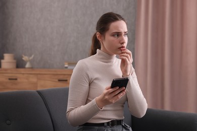 Photo of Depressed woman calling hotline for mental health help on sofa at home