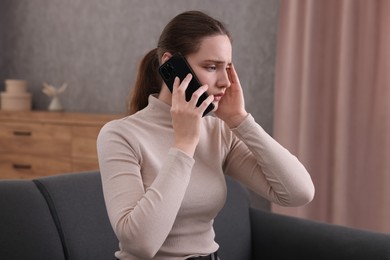 Photo of Depressed woman calling hotline for mental health help on sofa at home