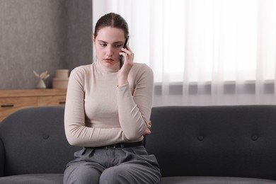 Photo of Depressed woman calling hotline for mental health help on sofa at home. Space for text